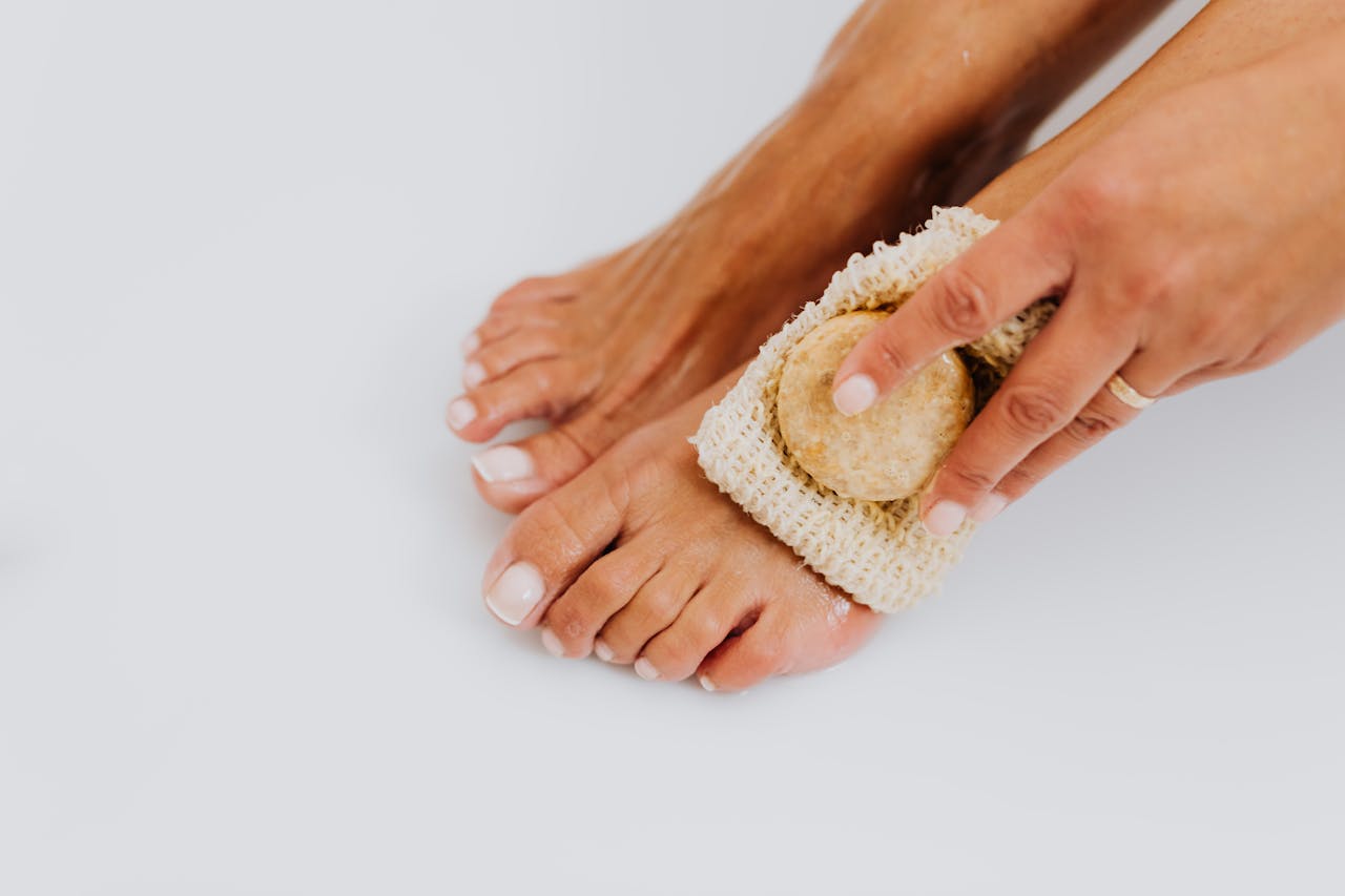 Close-up of a woman exfoliating her feet with a pumice stone and scrub pad, emphasizing personal care and hygiene.